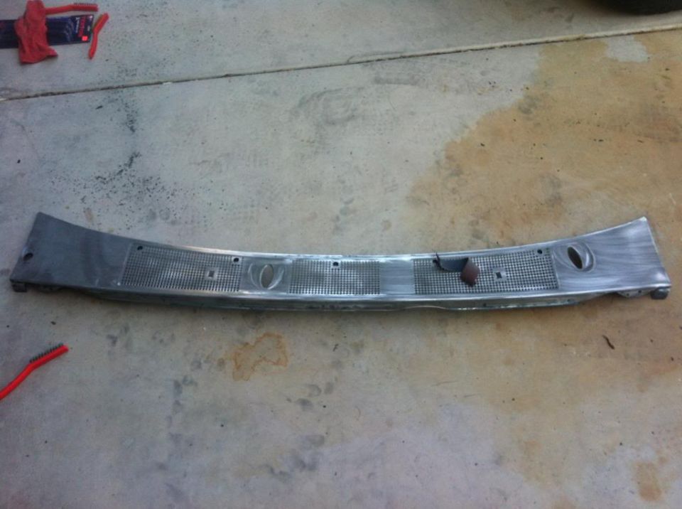 Metal windshield wiper cowl panel with grille pattern and oval indentations on concrete floor