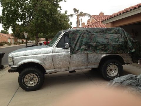 1994 Ford Bronco - This Ford Bronco is partially covered by a camouflage tarp, obscuring its full appearance.