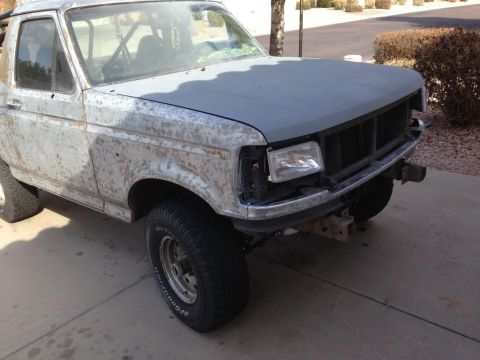 1994 Ford Bronco - This 1994 Ford Bronco shows significant body rust and a primer gray hood, with an interior roll cage visible.