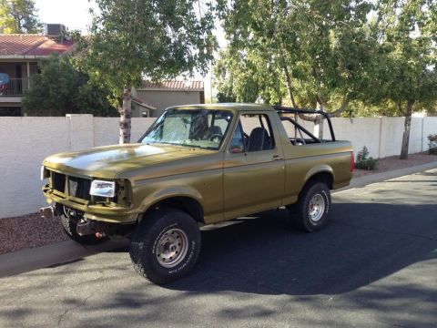 1994 Ford Bronco - This modified Ford Bronco features a roll cage and off-road tires, parked on a residential street.