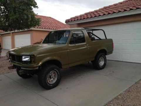 1994 Ford Bronco - This olive green Ford Bronco, likely from the early 1990s, is equipped with a roll cage and aftermarket wheels.