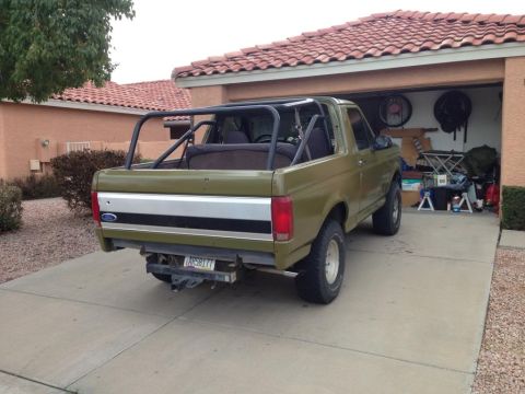 1994 Ford Bronco - Olive green Ford Bronco with a roll cage parked in a driveway.