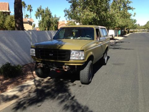 1994 Ford Bronco - This modified Ford Bronco is parked on a residential street under a clear blue sky.