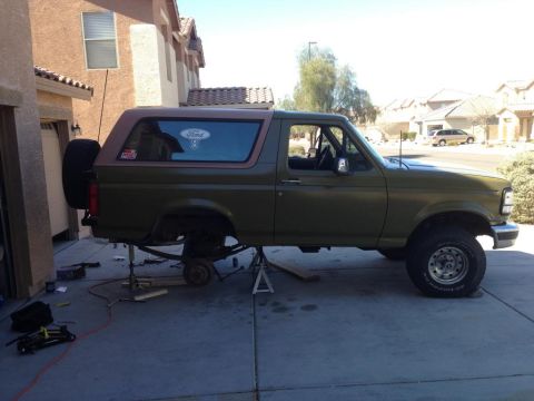 1994 Ford Bronco - A green Ford Bronco is undergoing maintenance, lifted on jack stands with its rear axle disassembled.