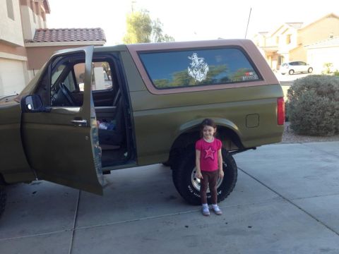 1994 Ford Bronco - A 1994 Ford Bronco is shown with its doors open, a young girl standing beside the large rear tire.