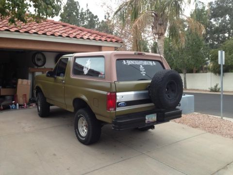1994 Ford Bronco - This 1994 Ford Bronco features a two-tone paint scheme and a spare tire mounted on the rear, with a website sticker on the back window.