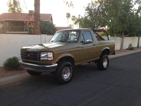 1994 Ford Bronco - This olive green Ford Bronco is shown from a three-quarter front angle, parked on a street.