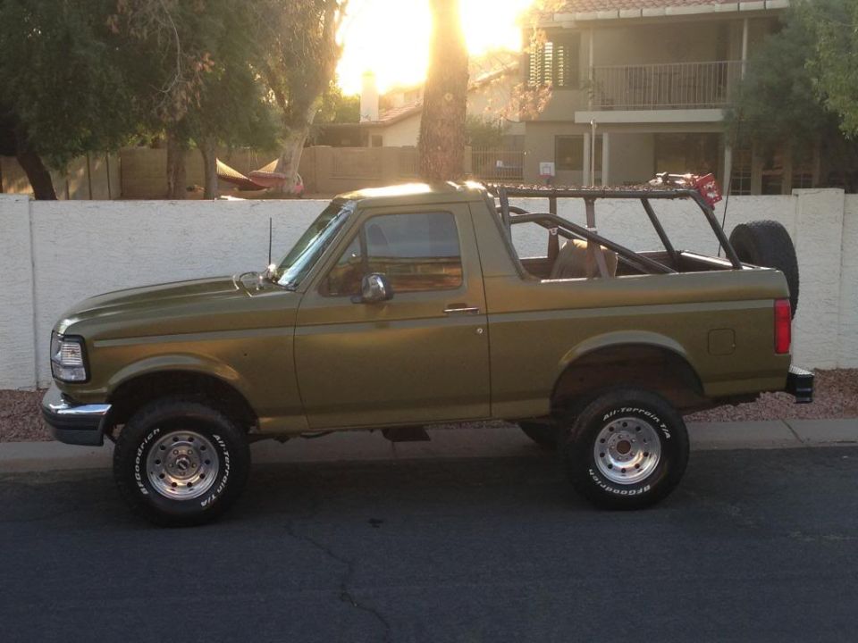 Olive green 1994 Ford Bronco side view with roll cage and spare tire