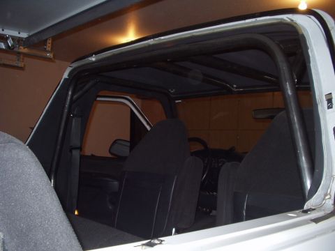 1993 Ford Bronco - The interior of a vehicle is visible, a prominent black roll cage structure and black upholstery on the seats.