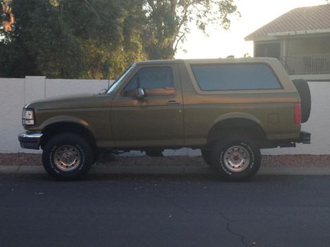 1994 Ford Bronco - This 1994 Ford Bronco is shown from the side, parked on a street with a house and trees in the background.