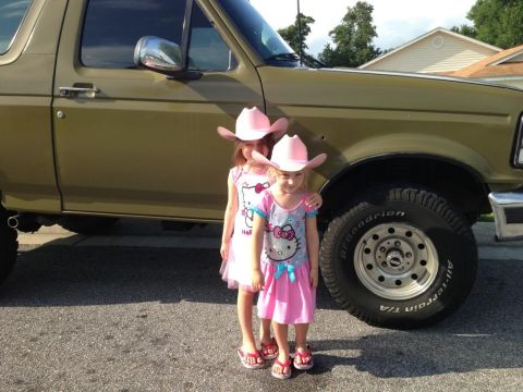 1994 Ford Bronco - Two young girls in pink cowboy hats and Hello Kitty dresses pose next to a large olive green SUV.