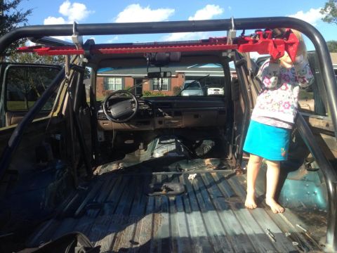 1994 Ford Bronco - The interior of a modified SUV shows a roll cage and a stripped cargo area, with a child standing inside.
