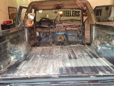1994 Ford Bronco - The interior of a truck is shown with the bed and cab disassembled, revealing the bare metal floor and dashboard components.