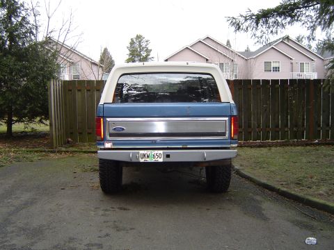 1989 Ford Bronco - The rear of a blue Ford Bronco is parked in a driveway with houses and a fence in the background.