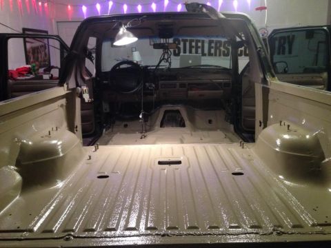 1994 Ford Bronco - Interior view of a tan Ford Bronco, showing the dashboard and empty bed, with lights overhead.
