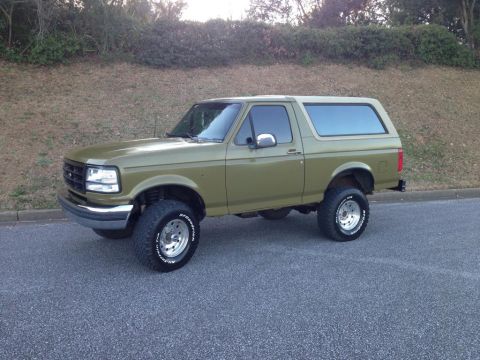 1994 Ford Bronco - This lifted Ford Bronco is shown from a three-quarter front view, highlighting its off-road tires and olive green paint.