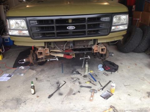 1994 Ford Bronco - Front end of a 1992 Ford Bronco undergoing suspension repairs, with tools scattered on the garage floor.