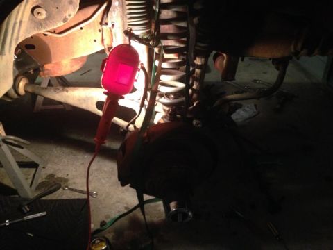 1994 Ford Bronco - Close-up view of a vehicle's underbody suspension and brake assembly, illuminated by a red work light.