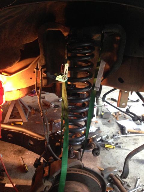 1994 Ford Bronco - Close-up of a vehicle's suspension system, showing a coil spring secured with straps.