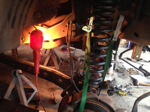 1994 Ford Bronco - Close-up view of a vehicle's suspension system undergoing repair, with a coil spring secured by straps and a red work light providing illum…