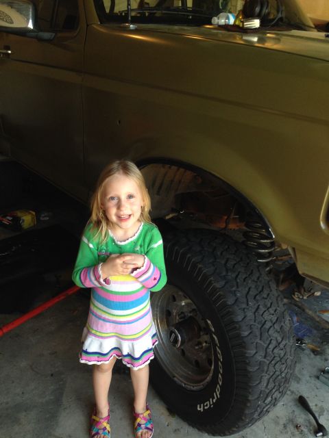 1994 Ford Bronco - A young girl poses next to the side of a 1994 Ford Bronco, showing its large tire and suspension.