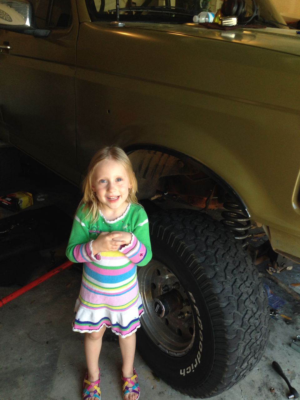 Girl in striped dress stands by the front fender and large tire of a 1994 Ford Bronco
