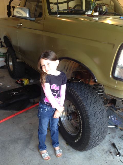 1994 Ford Bronco - A young girl poses next to a lifted truck in a garage setting, with the vehicle's suspension visible.