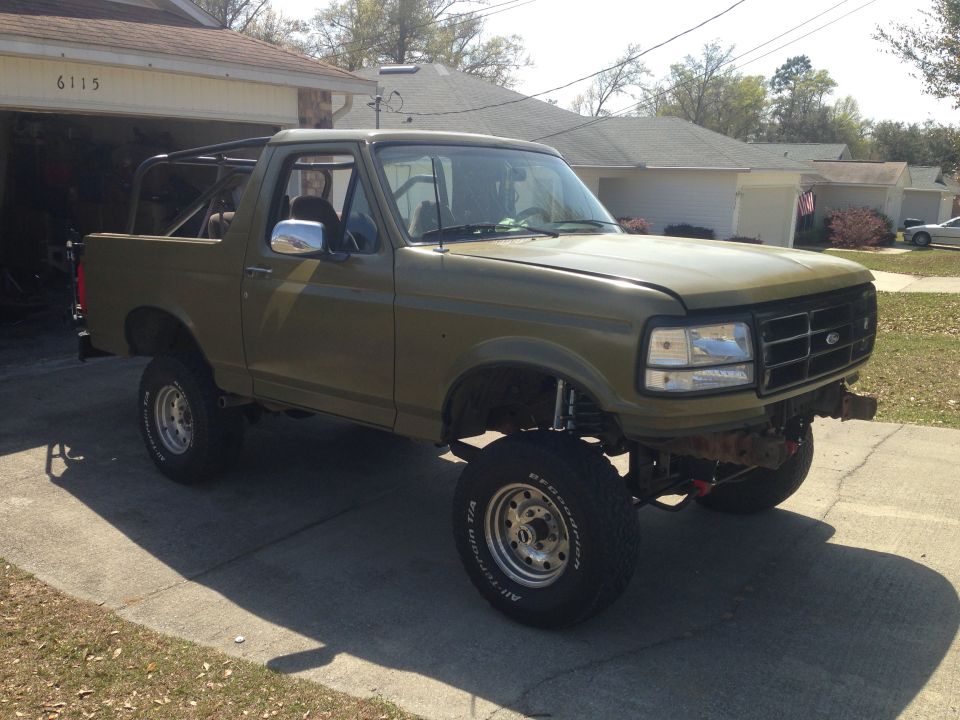 Olive green 1994 Ford Bronco with aftermarket roll cage and lifted suspension parked in driveway