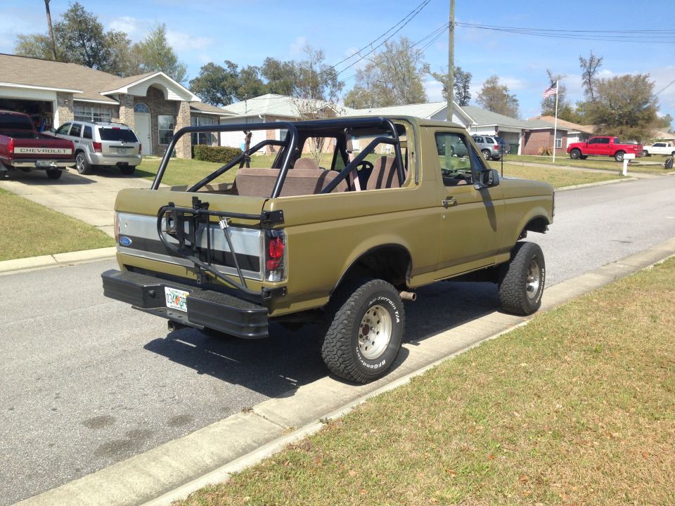 Olive green 1992 Ford Bronco with roll cage, lifted, parked on curb