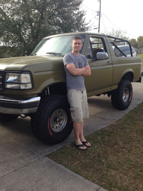 1994 Ford Bronco - A man poses with a modified Ford Bronco, a custom roll cage and oversized off-road tires.