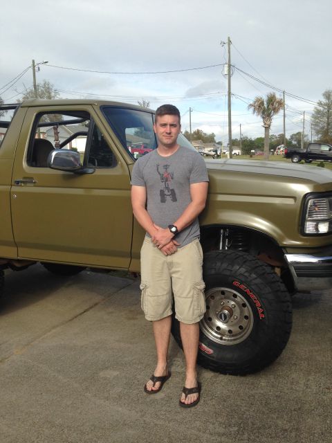 1994 Ford Bronco - A man stands beside a lifted 1994 Ford Bronco, its off-road modifications.