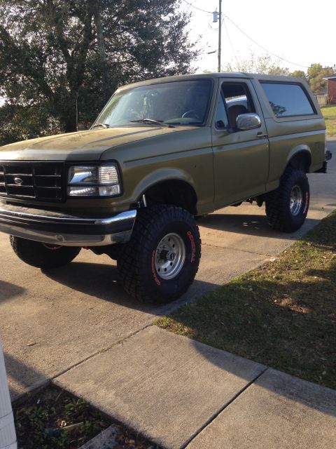 1994 Ford Bronco - Olive green 1994 Ford Bronco lifted with large tires sits on a concrete driveway.