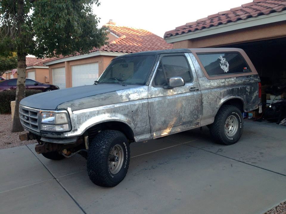 Ford Bronco with weathered body panels and aftermarket wheels parked in a driveway