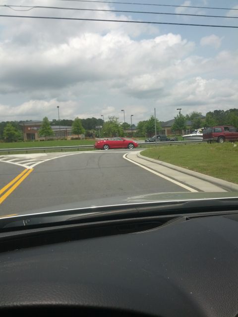 1979 Ford F-150 - A red convertible is seen driving on a road with other vehicles in the background under a cloudy sky.