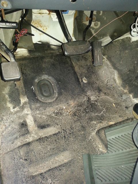1992 Ford Bronco - The dirty interior floor of a vehicle shows pedals and wiring, with a visible brake release lever.