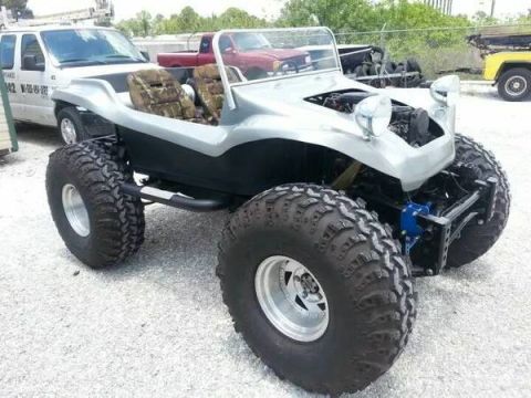 1987 Suzuki Samurai - Custom buggy with oversized tires and camouflage seats sits parked outdoors.