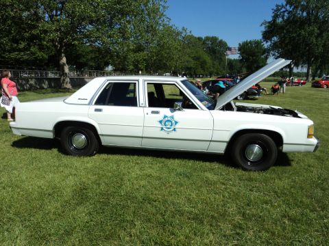 2004 Mercury Grand Marquis - A white sedan, possibly a former police vehicle, is displayed outdoors with its hood open.