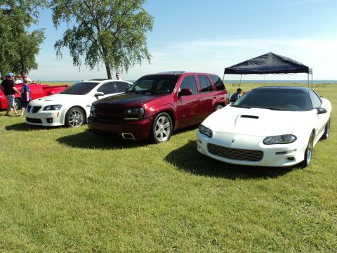 2004 Mercury Grand Marquis - A white Chevrolet Camaro is parked on a grassy field alongside other vehicles under a sunny sky.