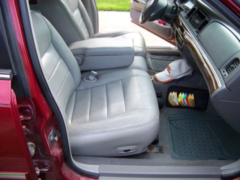1999 Mercury Grand Marquis - The interior of a red car features light grey leather seats, a center console, and a dashboard with wood trim. A CD case and a hat are visi…