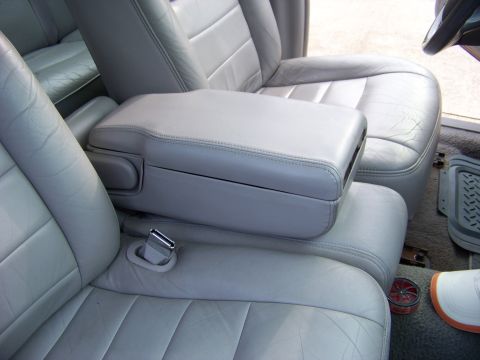 1999 Mercury Grand Marquis - The interior of a vehicle features light gray leather seats and a center console with a visible seatbelt buckle.