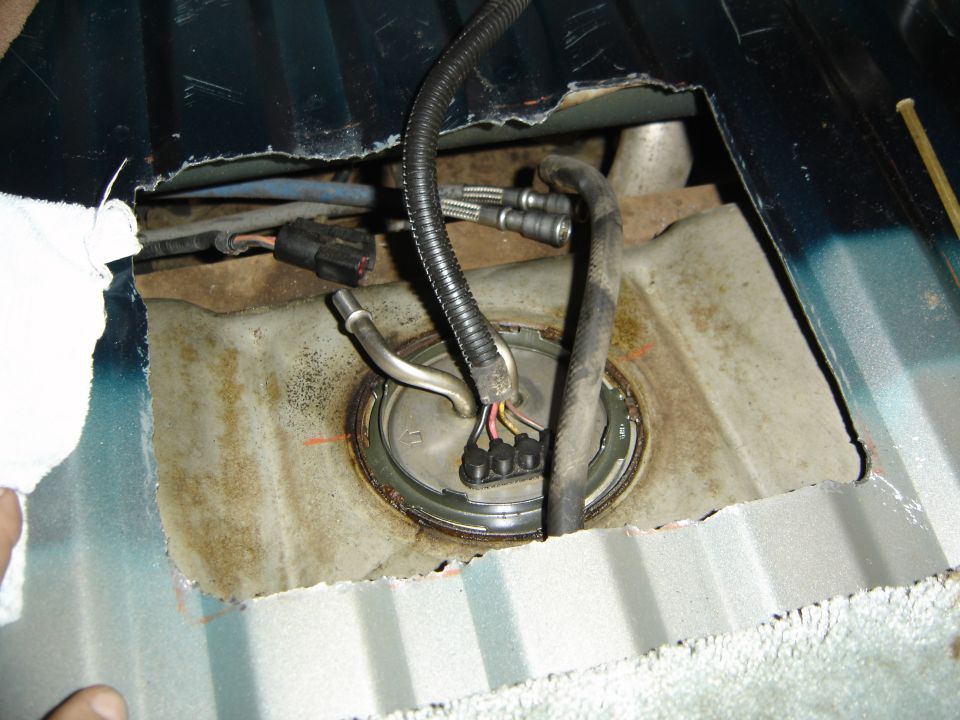 Fuel pump assembly removed from vehicle floor, showing wiring and fuel lines
