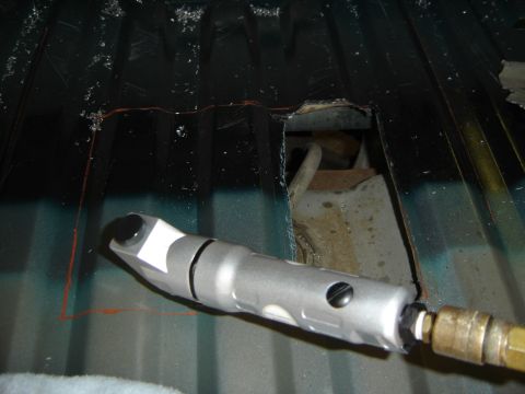 1996 Ford Bronco - An access hole being cut through a ribbed dark green sheet-metal floor pan, with the opening marked out in orange marker and metal shavings…