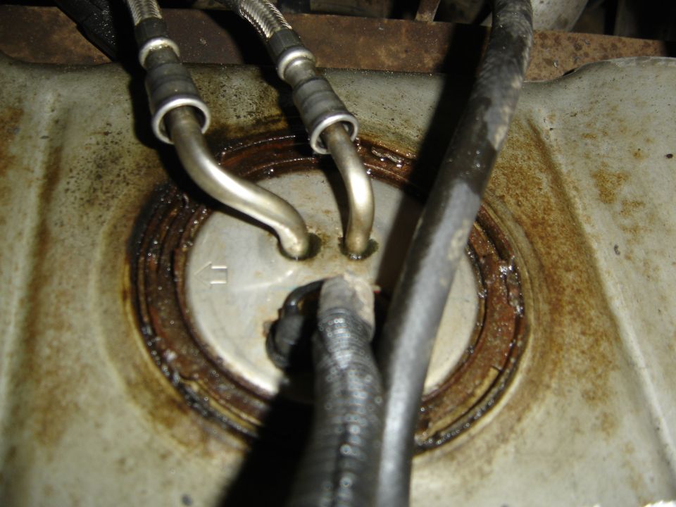 Fuel pump assembly with metal lines and rubber hose, showing rust and grime
