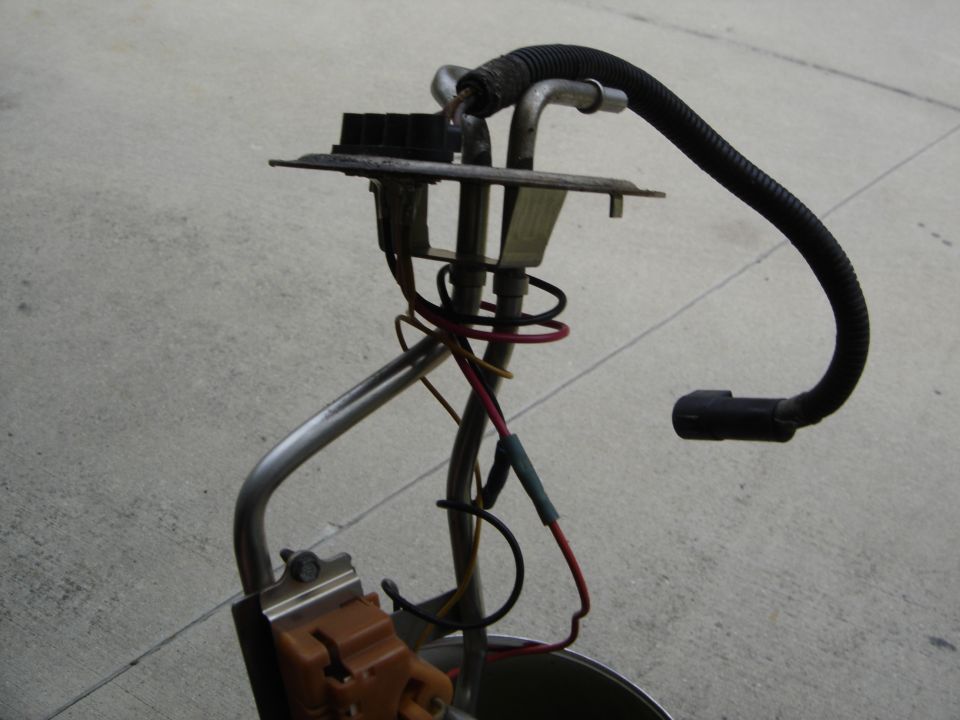 Fuel pump assembly with wiring and hoses, resting on a concrete surface