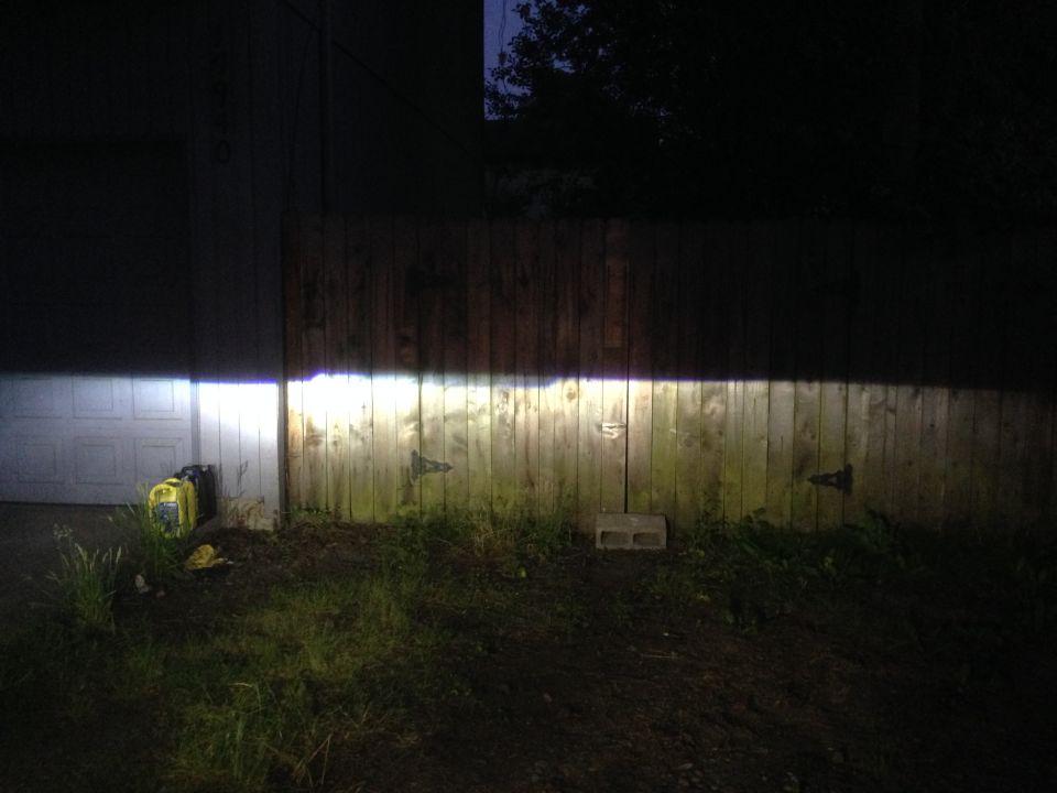Headlights illuminate a wooden fence at night, with a yellow generator visible to the left