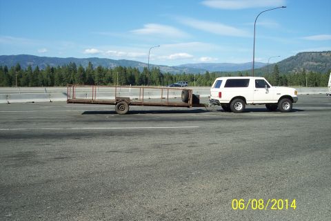 1990 Ford Bronco - A white 1990 Ford Bronco is seen from the side, towing a utility trailer on a highway.