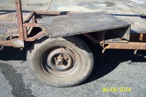 1990 Ford Bronco - This photo shows a close-up of a rusty trailer wheel and part of its frame, with a wooden plank resting on top.