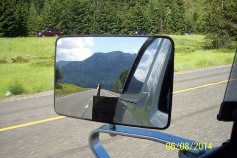 1990 Ford Bronco - Reflection in the side mirror captures a scenic mountain road with trees lining the highway.