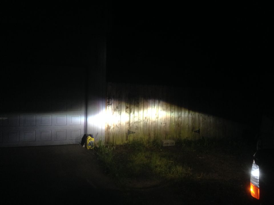 Headlights project a bright beam onto a wooden fence and garage door at night