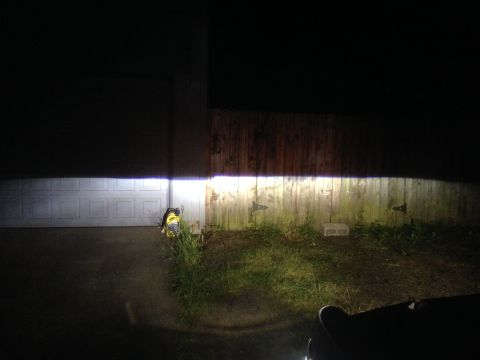1992 Ford F-150 - The bright beams from the vehicle's headlights illuminate a wooden fence and a garage door in the darkness.
